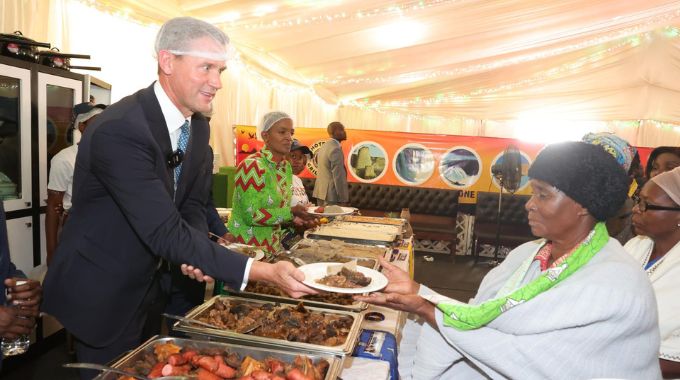 British Ambassador to Zimbabwe Mr Pete Vowles serve food to guests in First Lady Dr Auxillia Mnangagwa’s traditional foods kitchen at the 64th ZITF in Bulawayo