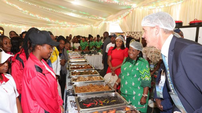 British Ambassador Mr Pete Vowles interacts with girls who attended nhanga programme while serving food to guests in First Lady Dr Auxillia Mnangagwa’s traditional foods kitchen at the 64th ZITF in Bulawayo