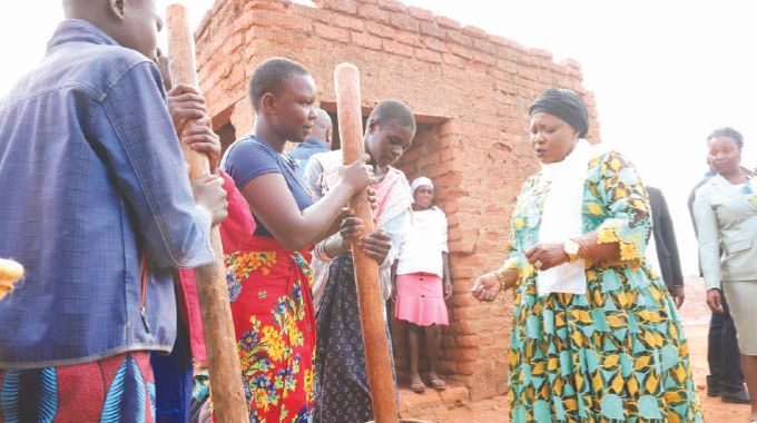 First Lady Dr Auxillia Mnangagwa teaches girls how to use the traditional mortar and pestle to prepare peanut butter and mealie meal from traditional grains during a nhanga programme she organized in Chingwizi on Tuesday