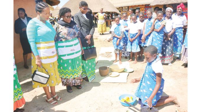 Princess Lindiwe of Eswatini, Minister for Mashonaland East and Devolution Dr Aplonia Munzverengwi and Ms Grace Neo Likando who was representing Zambian Ambassador’s wife Mrs Livune observe as one of the girls demonstrates how to prepare nhopi, which is one of Zimbabwe’s traditional dishes during a nhanga programme organised by First Lady Dr Auxillia Mnangagwa at the Heritage Village in Harare on Sunday