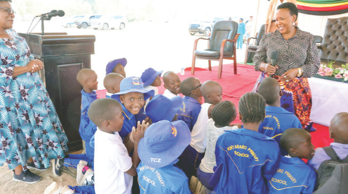 First Lady Dr Auxillia Mnangagwa teaches children how to thank the traditional way using totems, while Minister of State and Devolution for Mashonaland East Aplonia Munzverengwi looks on during a school feeding programme in Chivhu yesterday. – Pictures: John Manzongo