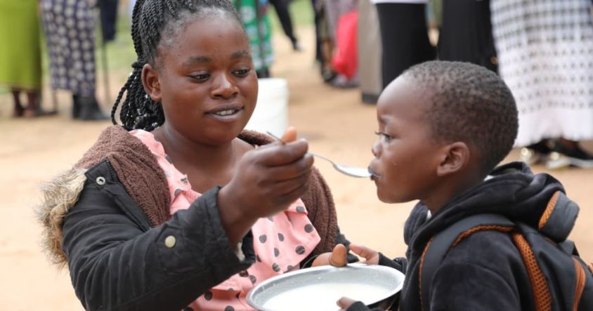 A mother feeds her child porridge during the launch of the oversubscribed Toddlers’ Warm Bowl Project in Epworth